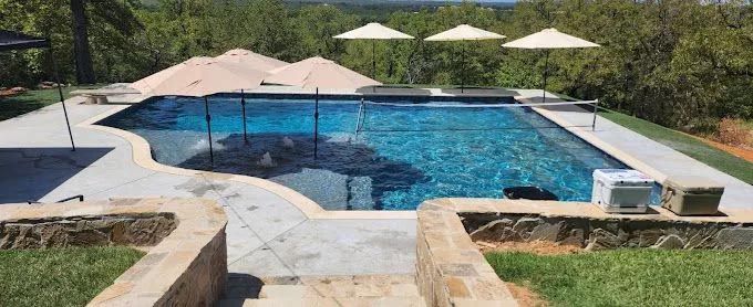 A large swimming pool surrounded by umbrellas and trees.