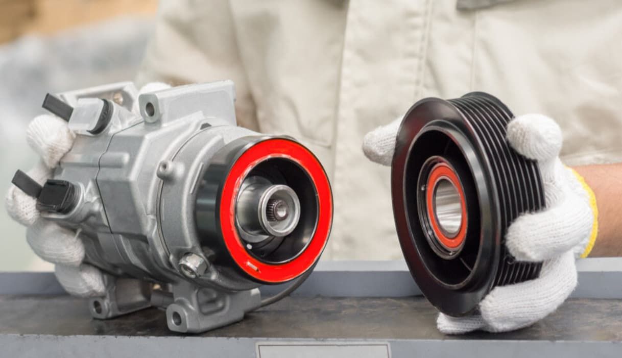 A Person Is Holding A Compressor And A Pulley In Their Hands — Bartons Auto Air Conditioning In Tolga, QLD