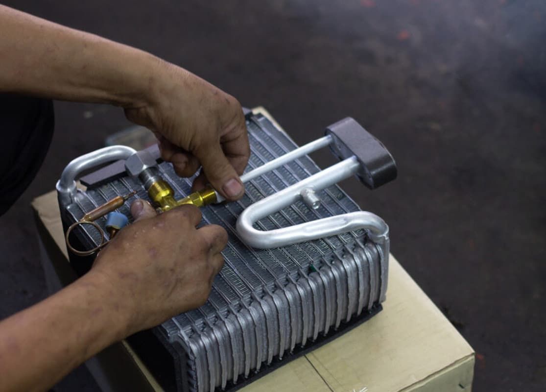 A Man Is Working On An Air Conditioner Coil With A Pair Of Pliers — Bartons Auto Air Conditioning In Tolga, QLD
