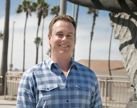 A man in a plaid shirt is smiling in front of a statue. Casey McKeon