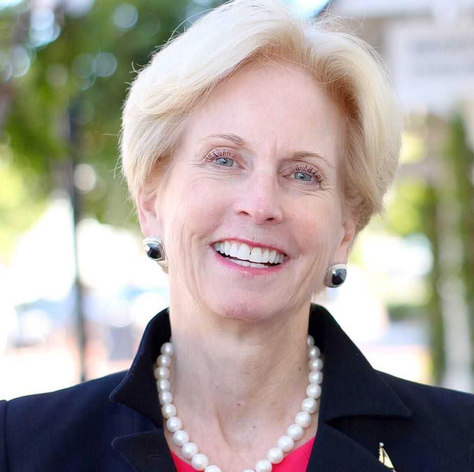 A woman wearing a pearl necklace and earrings is smiling for the camera. Diane Dixon