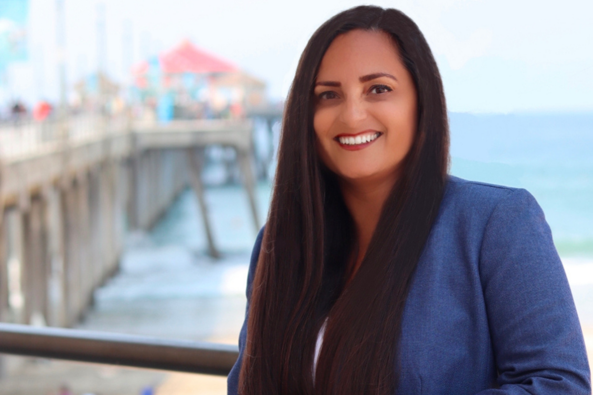 A woman with long hair is smiling in front of a pier. Gracey Van Der Mark