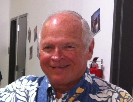 A man in a hawaiian shirt is smiling in front of a fire extinguisher. Jim Silva