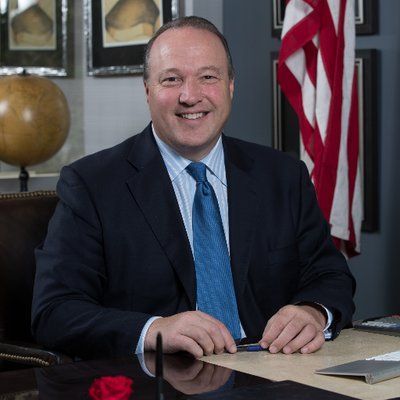A man in a suit and tie is sitting at a desk in front of an american flag. Scott Baugh