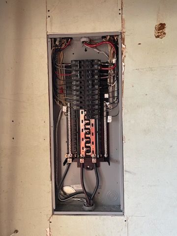Electrical panel in a wall opening, wires visible, black breakers, copper bars.