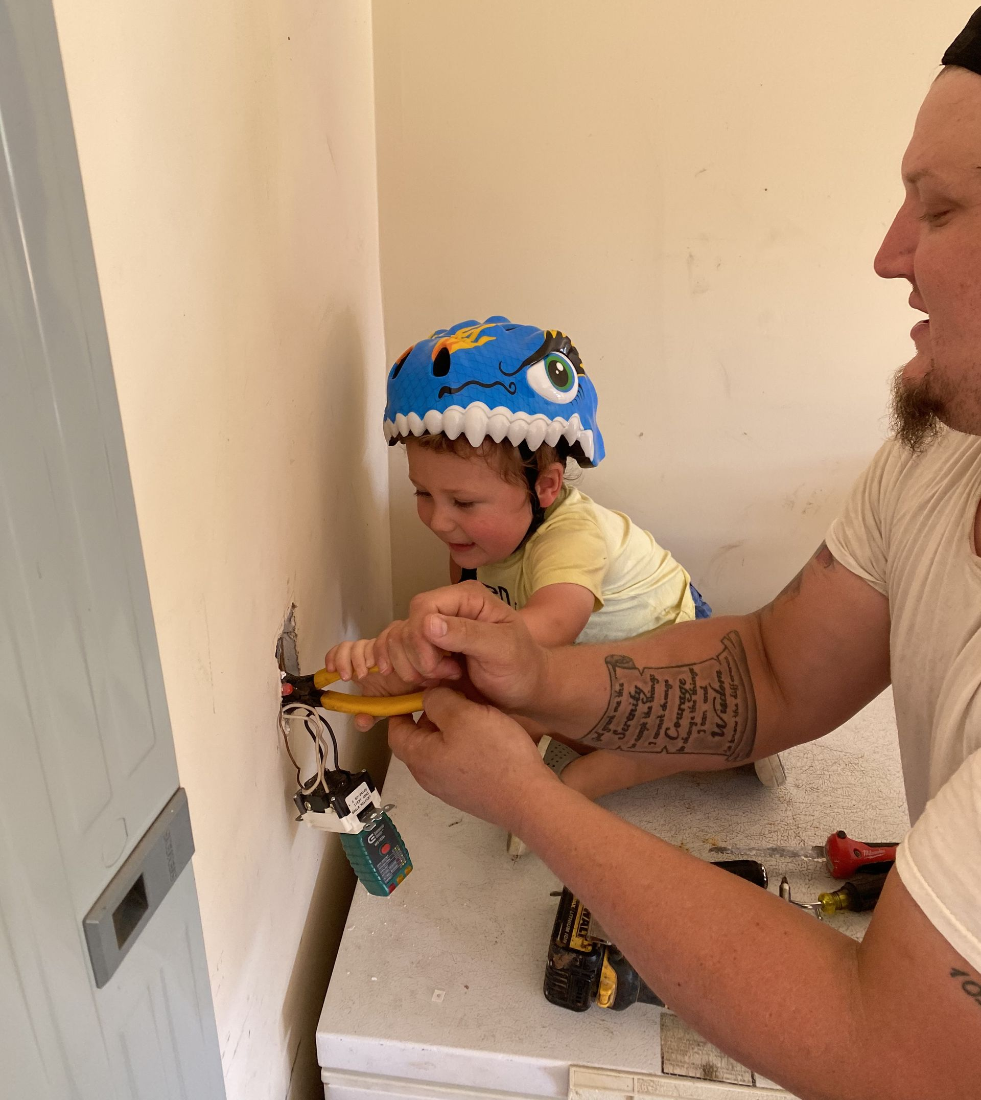 Man and child with dinosaur helmet work on electrical outlet.