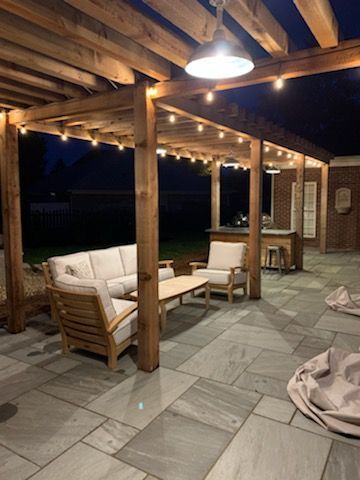 Outdoor patio with wooden pergola, string lights, seating, and bar.