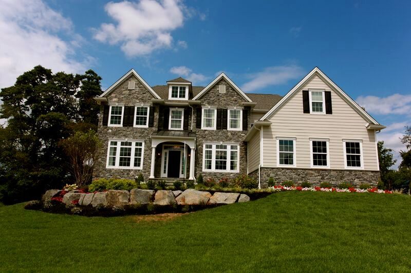 A large house with a lot of windows sits on top of a lush green hillside