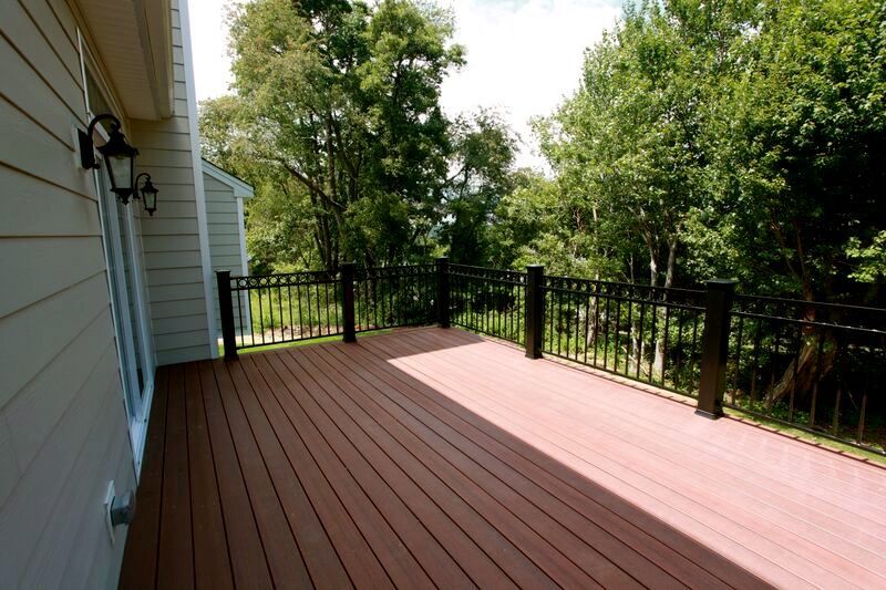 A wooden deck with a black railing and trees in the background