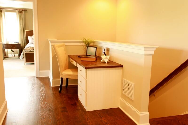 There is a desk in the corner of the room next to the stairs.