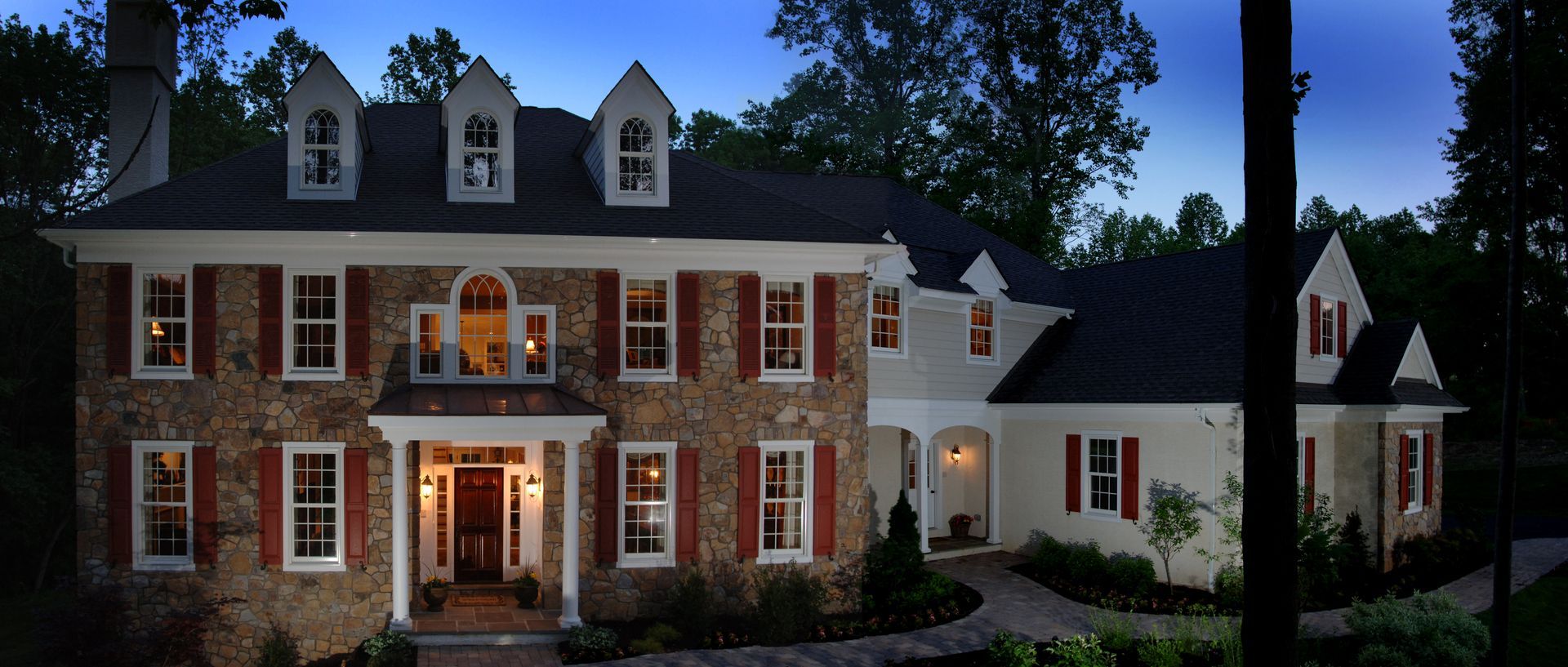 A large brick house with a black roof is lit up at night