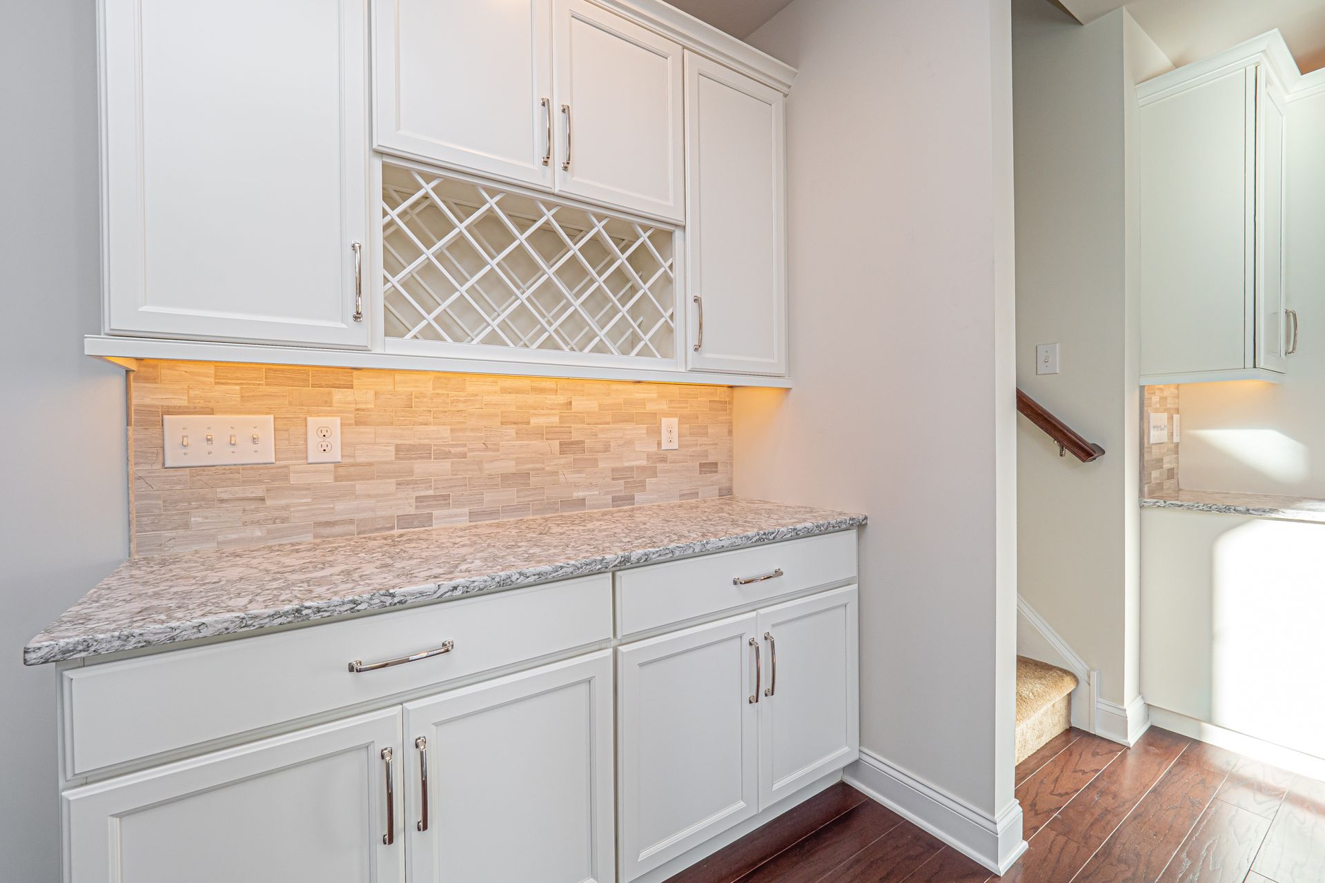 A kitchen with white cabinets , granite counter tops , and a wine rack.
