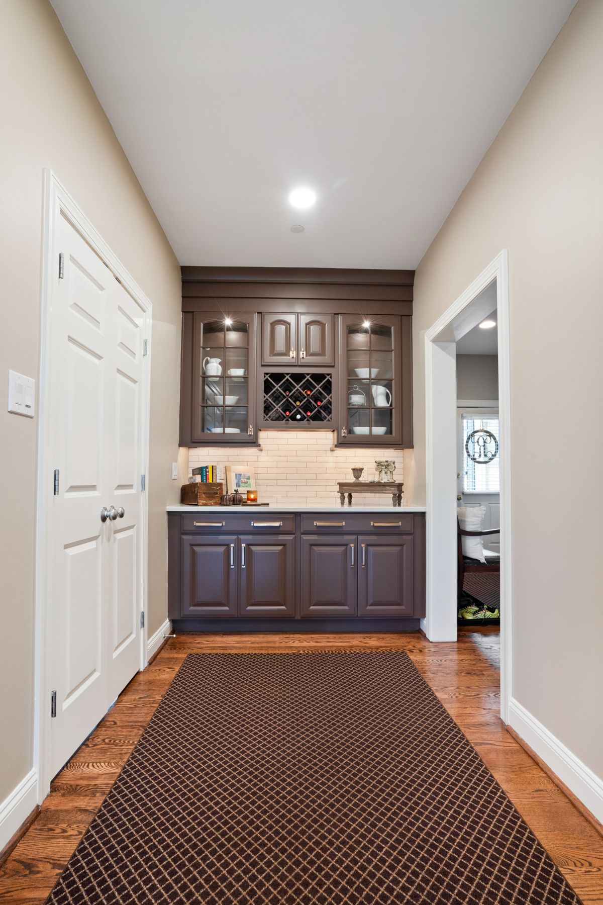 A hallway leading to a kitchen with brown cabinets and a wine rack