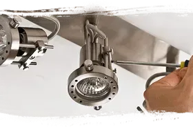 A person using a screwdriver to adjust a metallic spotlight fixture.