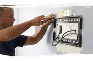 A person using a screwdriver to adjust a metallic spotlight fixture.