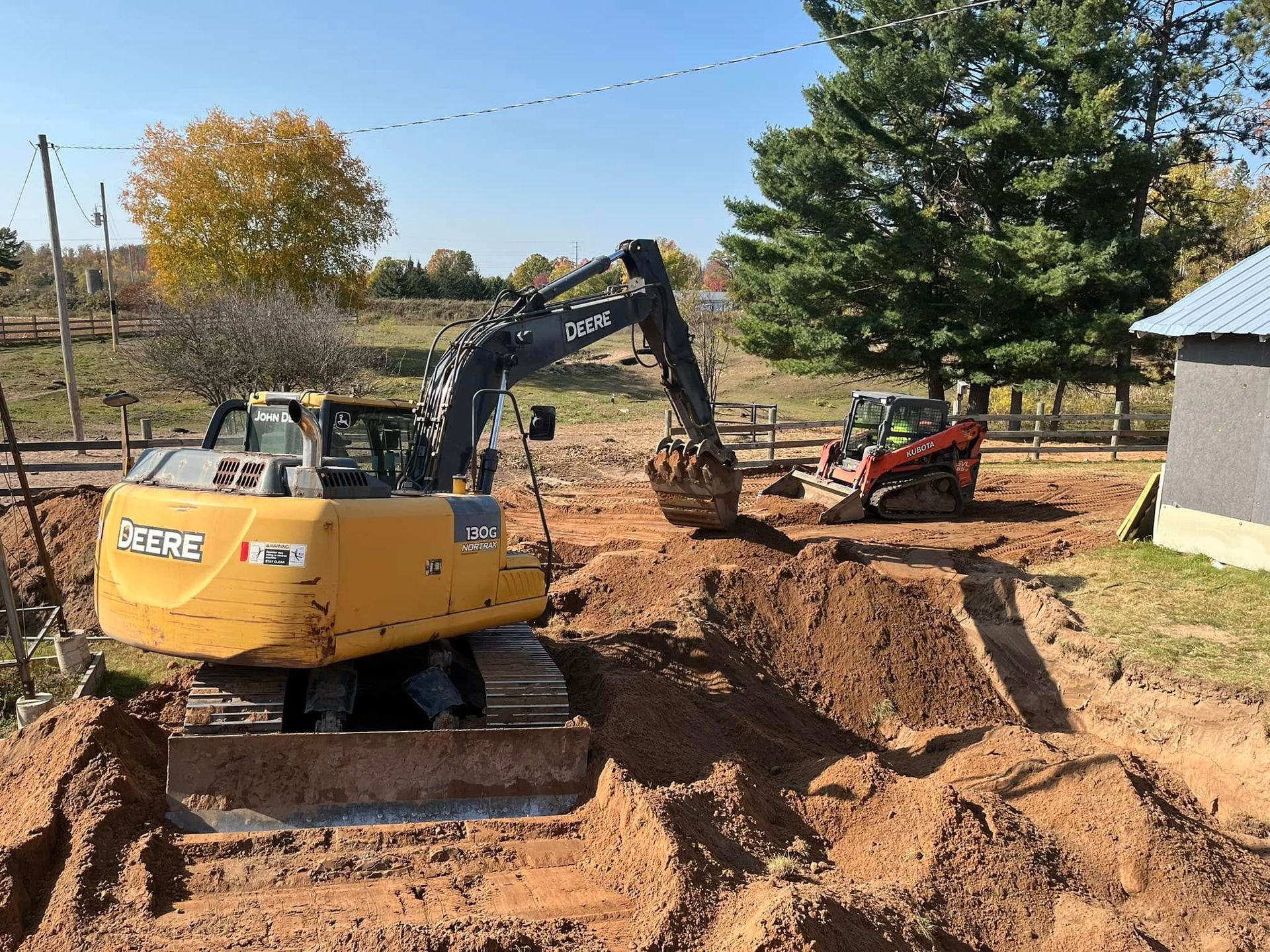A person in a gray shirt stands next to a flatbed truck loaded with large concrete pipes on a leaf-covered forest floor.