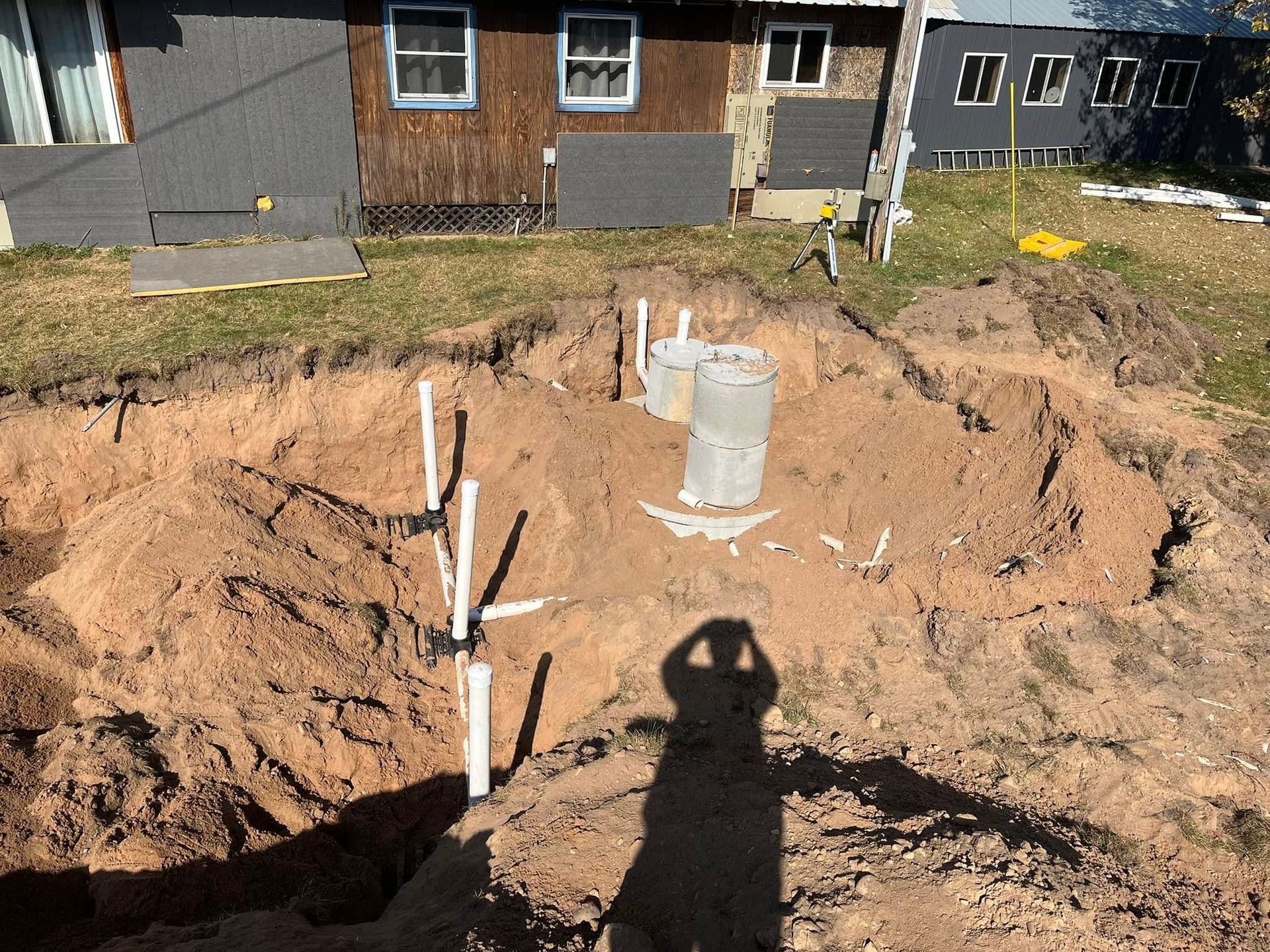 A smiling person in a dark green polo and black gloves holds papers while standing in a bright, plant-filled indoor space.