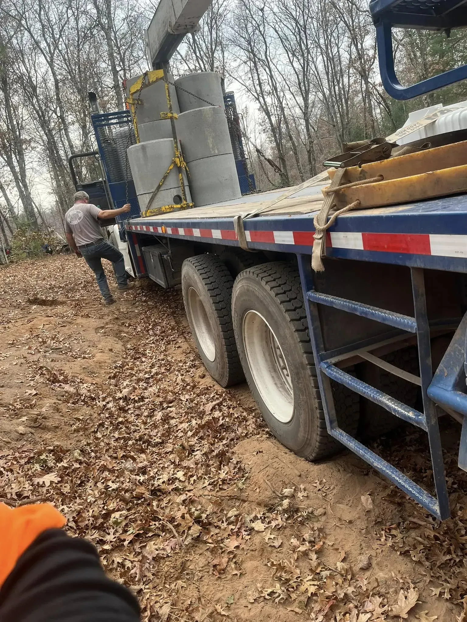 A smiling person in a dark green polo and black gloves holds papers while standing in a bright, plant-filled indoor space.