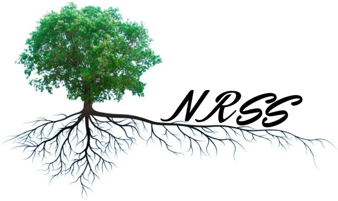 A smiling person in a dark green polo and black gloves holds papers while standing in a bright, plant-filled indoor space.