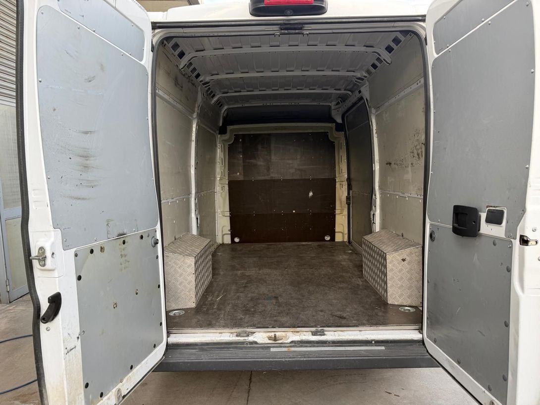 Interno aperto di un furgone merci con porte bianche e pavimento grigio vuoto, vista verso la parete posteriore.