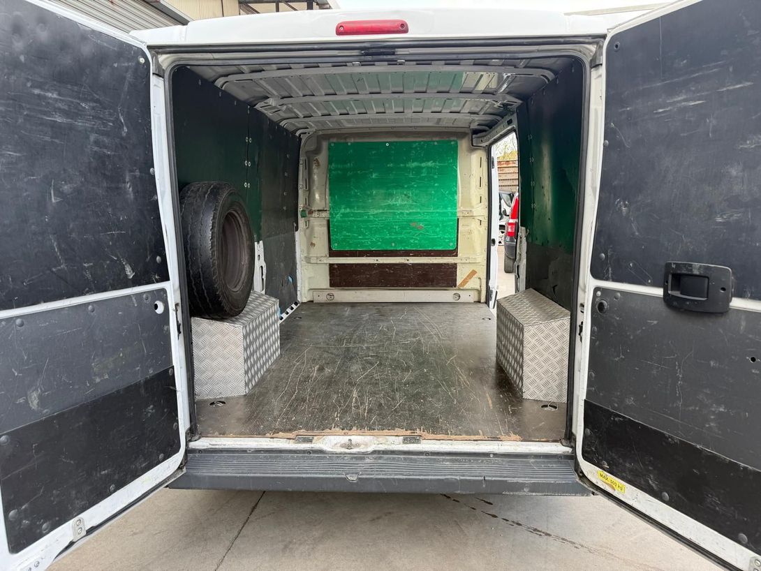 Interno di un furgone merci aperto con pareti rivestite in metallo e portellone posteriore che si apre su uno sfondo verde.