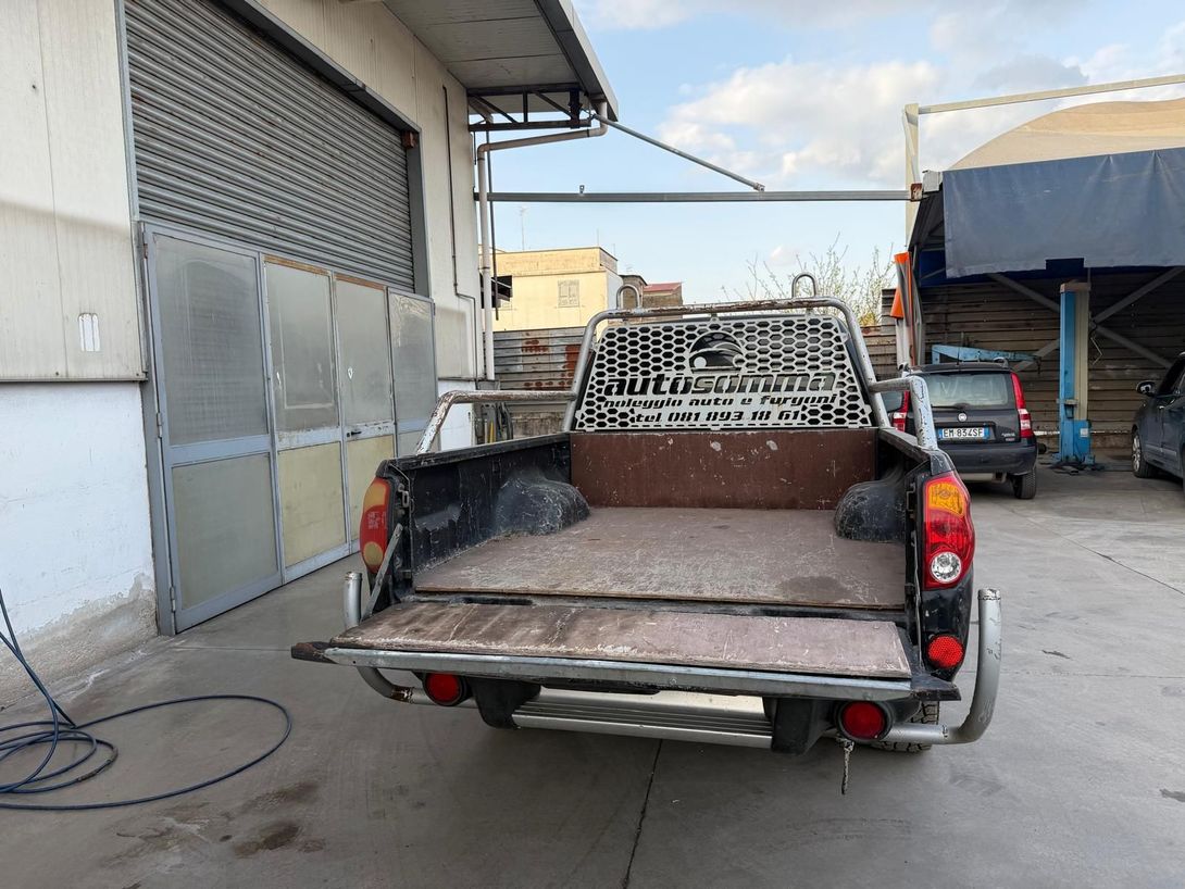 Un pick-up con cassone aperto è parcheggiato accanto a un edificio in una zona industriale.