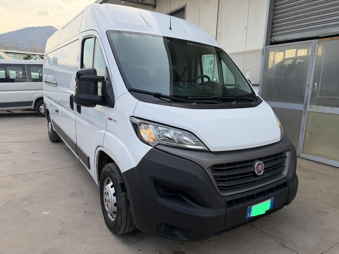 Furgone bianco parcheggiato all'aperto vicino a un edificio, vista frontale sinistra con paraurti e griglia neri.