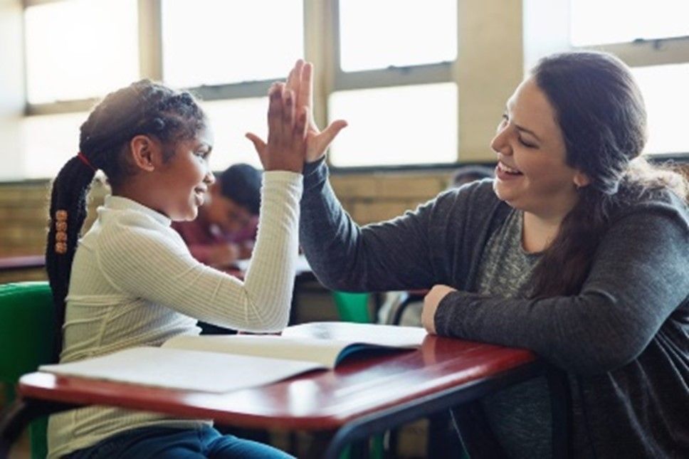 a woman is giving a child a high five in a classroom .