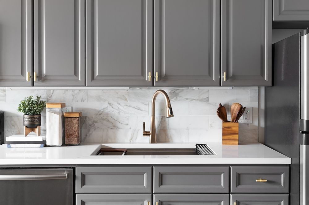 A kitchen with gray cabinets , stainless steel appliances , a sink and a refrigerator.