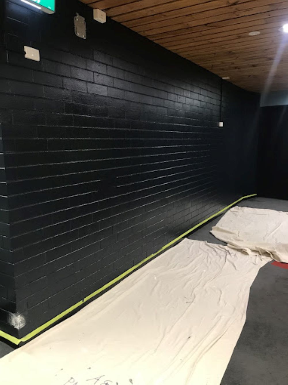 A Room With a Black Brick Wall and a White Tarp on the Floor — A&J Painting In Gungahlin, NT