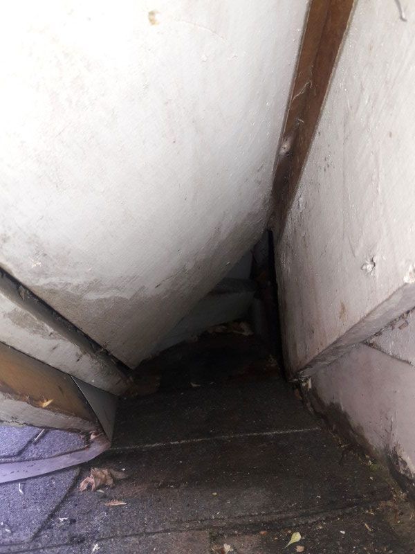Narrow, dark crawl space beneath a sloped roof. White walls, dark floor, debris.