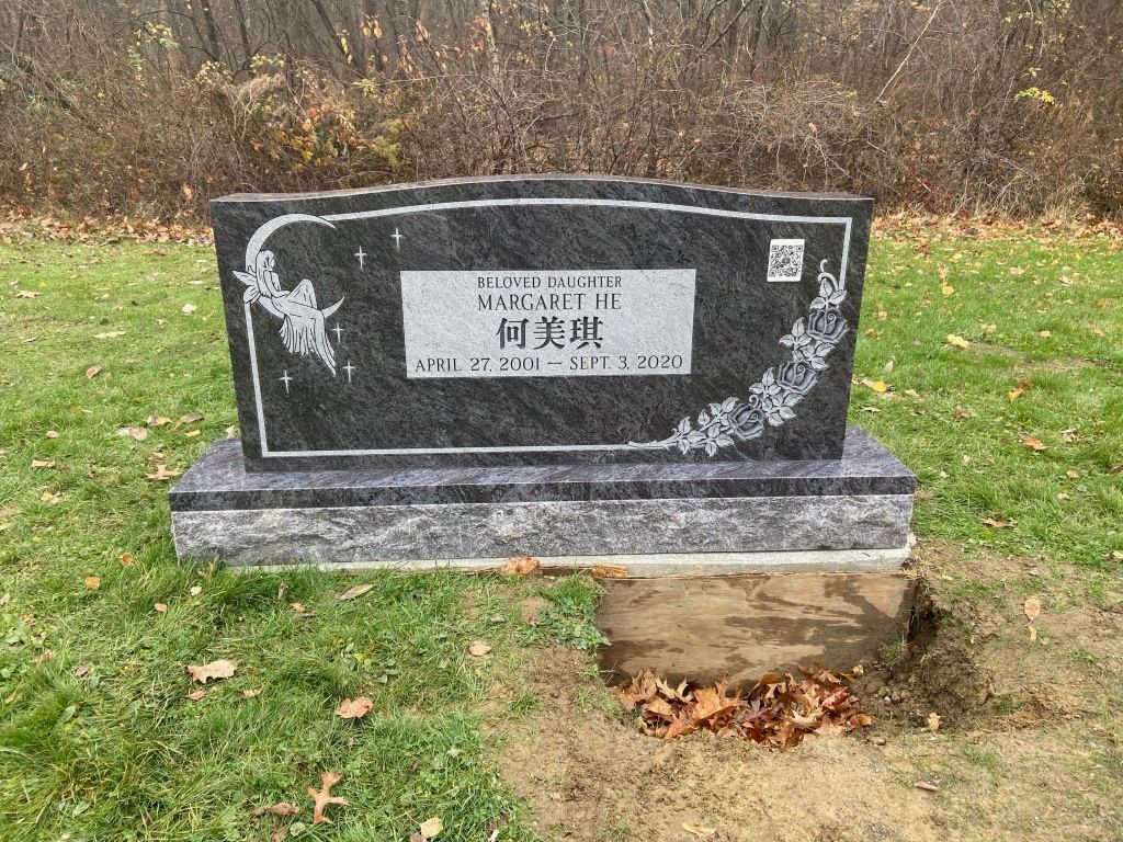 A black gravestone is sitting in the middle of a grassy field.