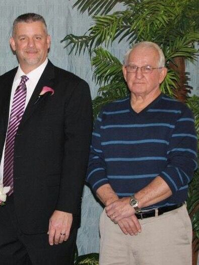 Two men standing next to each other in front of a palm tree
