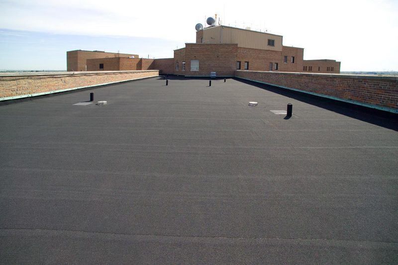 A black roof with a brick building in the background