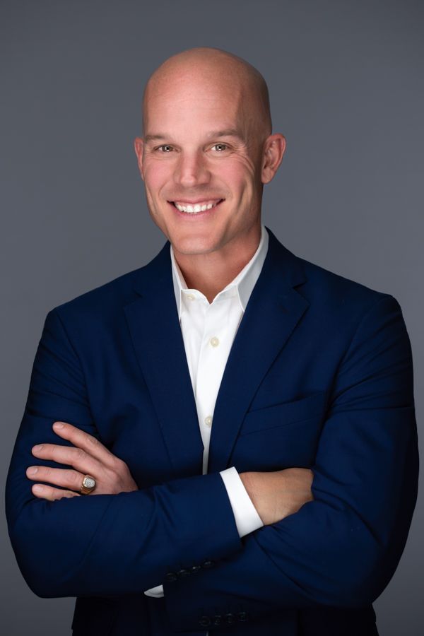 A bald man in a blue suit and white shirt is smiling with his arms crossed.