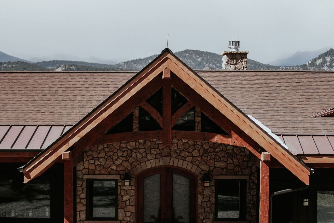 A large stone house with a wooden roof and mountains in the background.