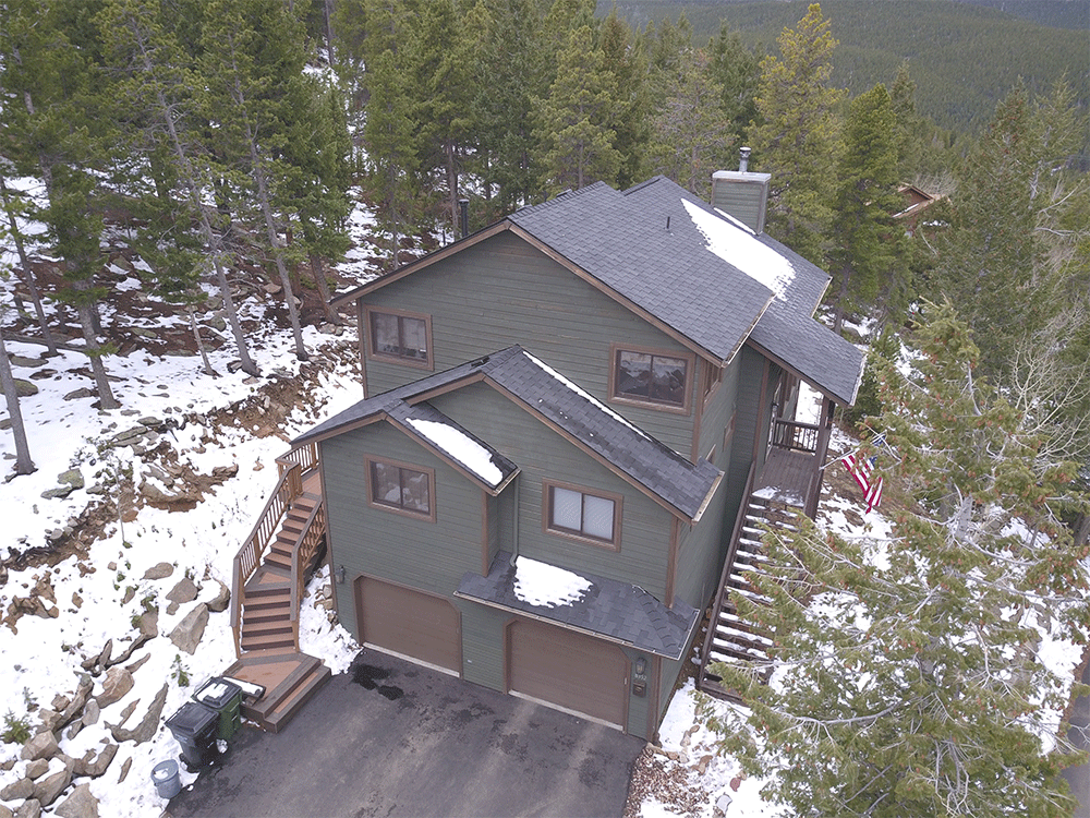 An aerial view of a house surrounded by snow covered trees