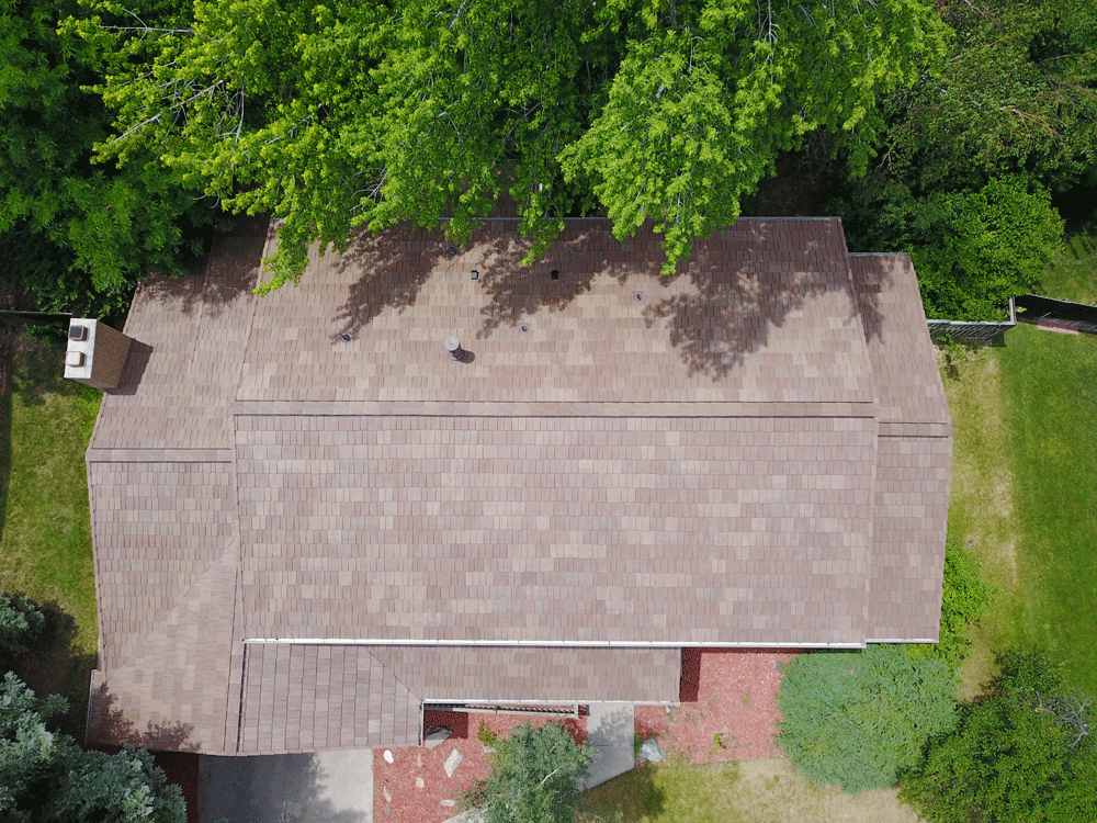 An aerial view of a house with a roof and trees in the background.