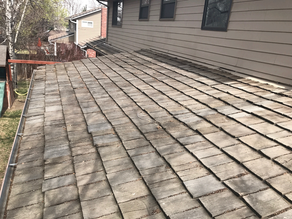 A roof with a lot of tiles on it and a house in the background.