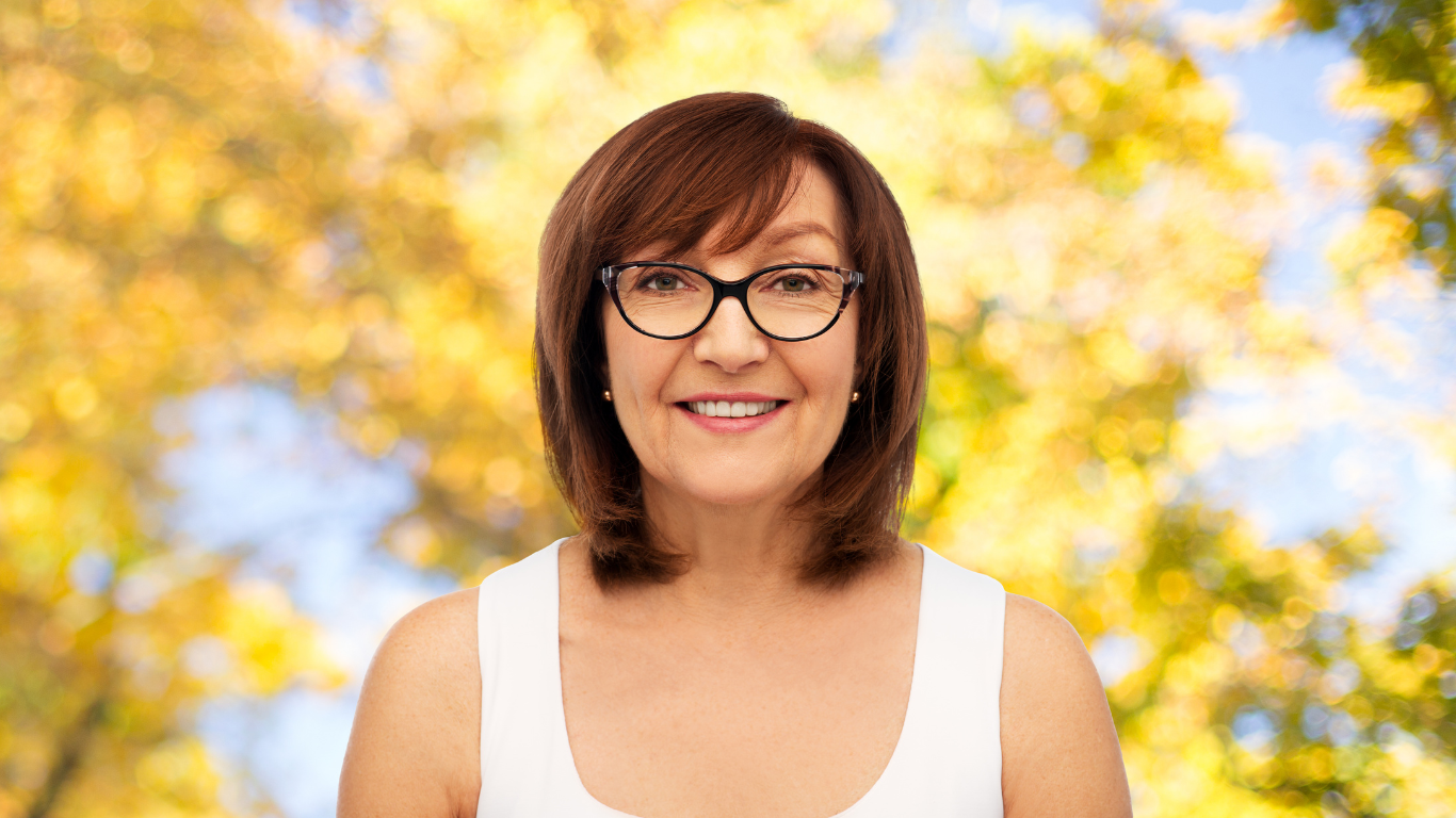 A woman wearing designer eyeglasses and a white tank top is smiling.