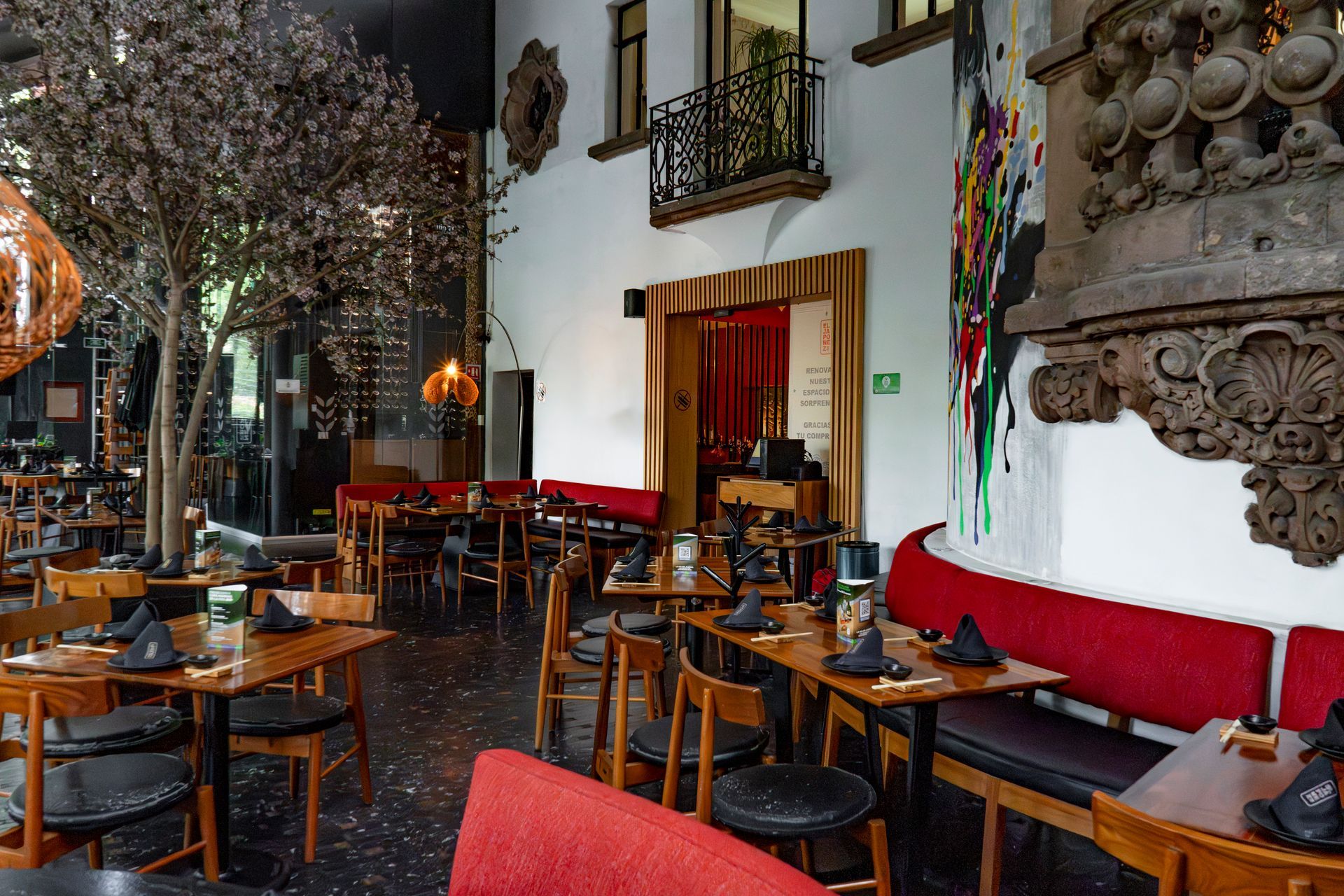 Interior acogedor de una cafetería con mesas de madera, bancos rojos y decoración de pared ornamentada.