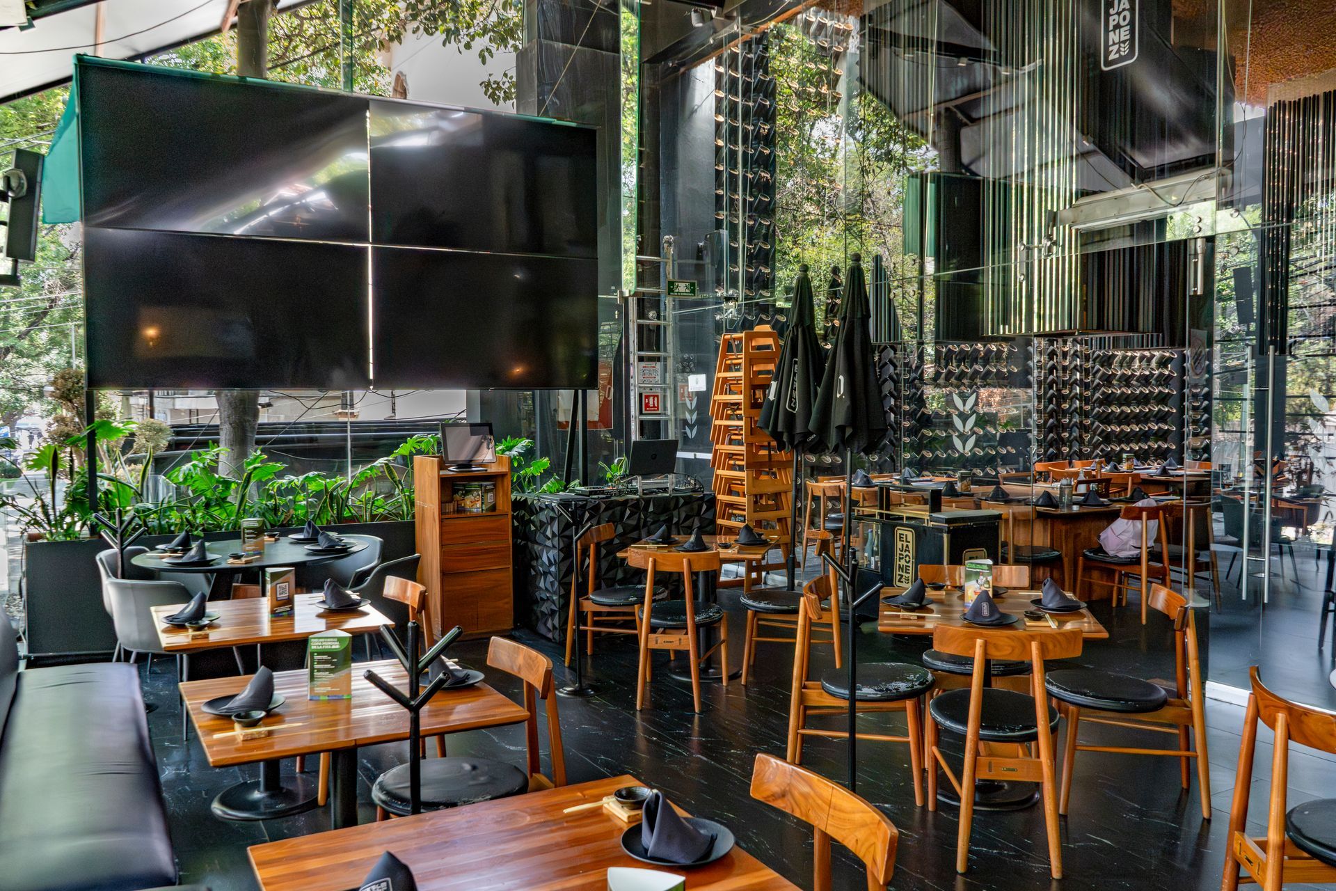 Interior de restaurante moderno con mesas de madera, sillas naranjas y grandes paredes con espejos.