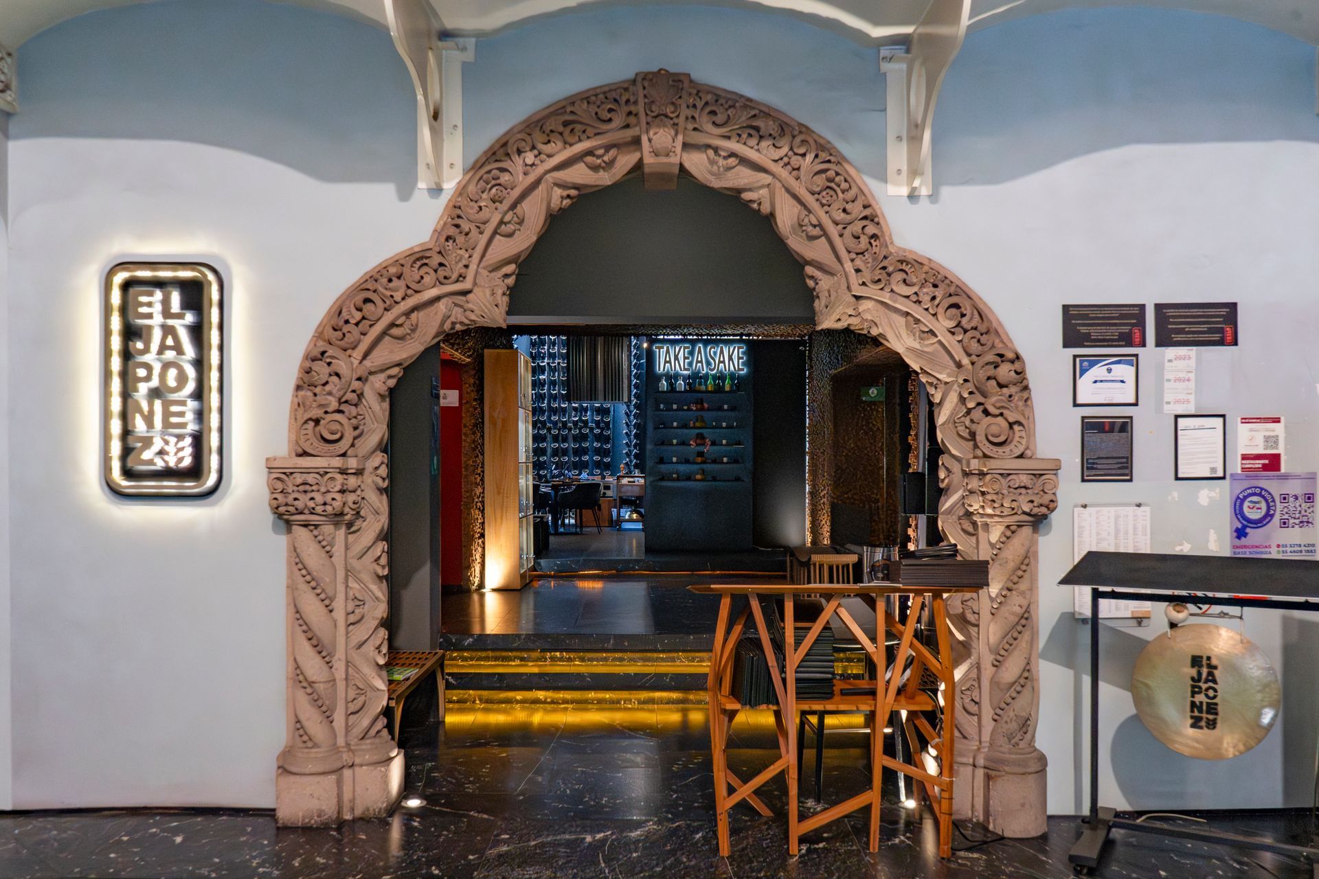 Arco ornamentado tallado que enmarca una puerta en un interior que recuerda a un museo, con señalización y vitrinas.