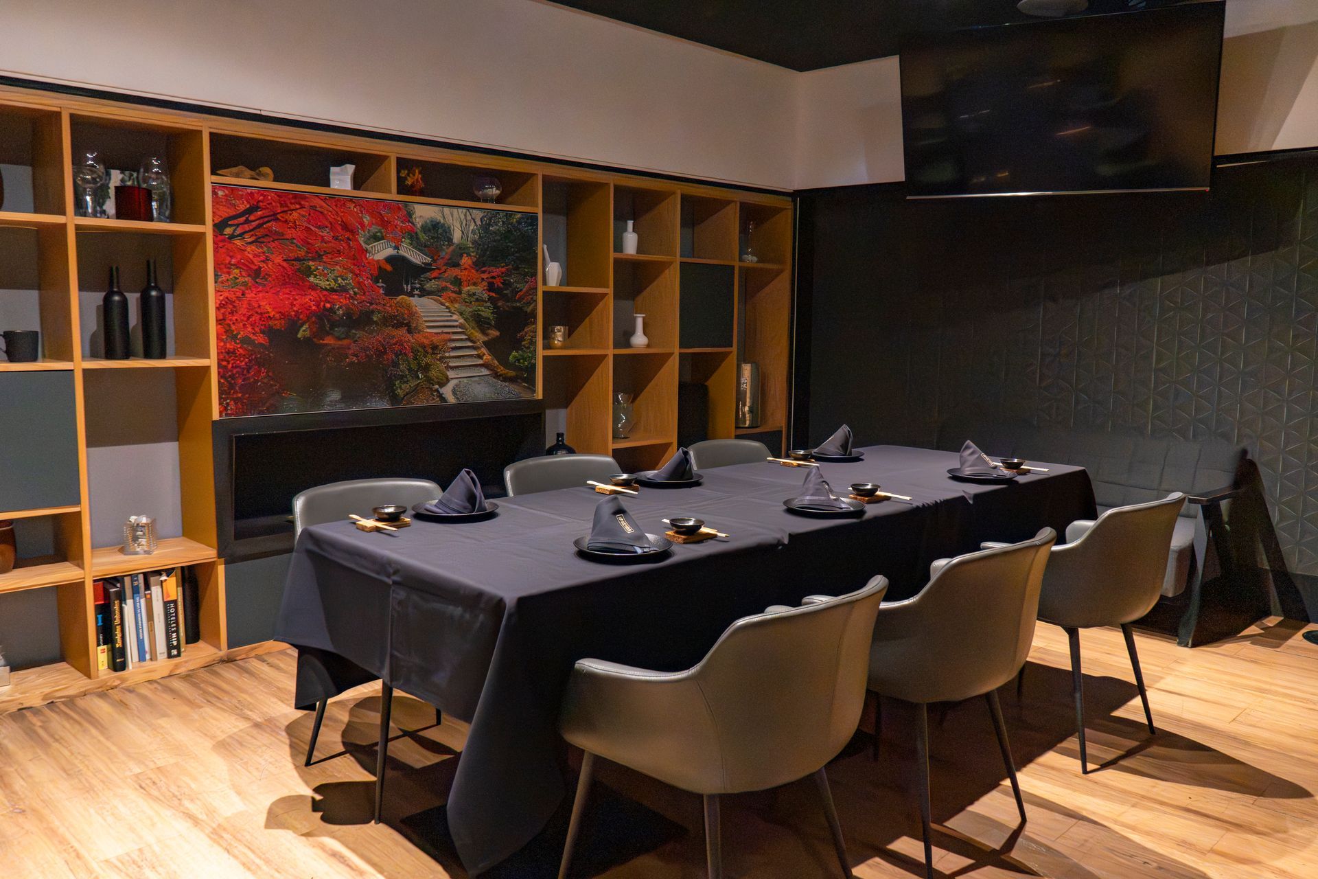 Comedor moderno con una mesa larga negra, sillas color canela, estantes de madera y una obra de arte roja en la pared.