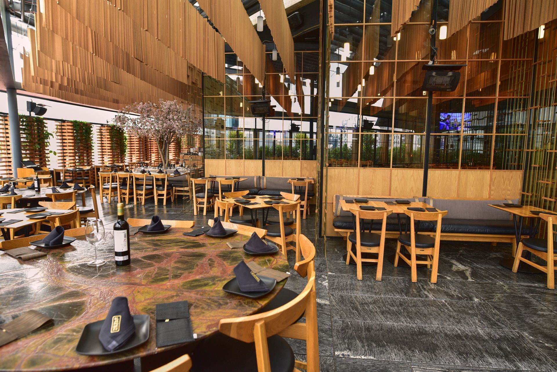 Comedor vacío de un restaurante con mesas de madera, sillas negras y un interior cálido de madera y cristal.