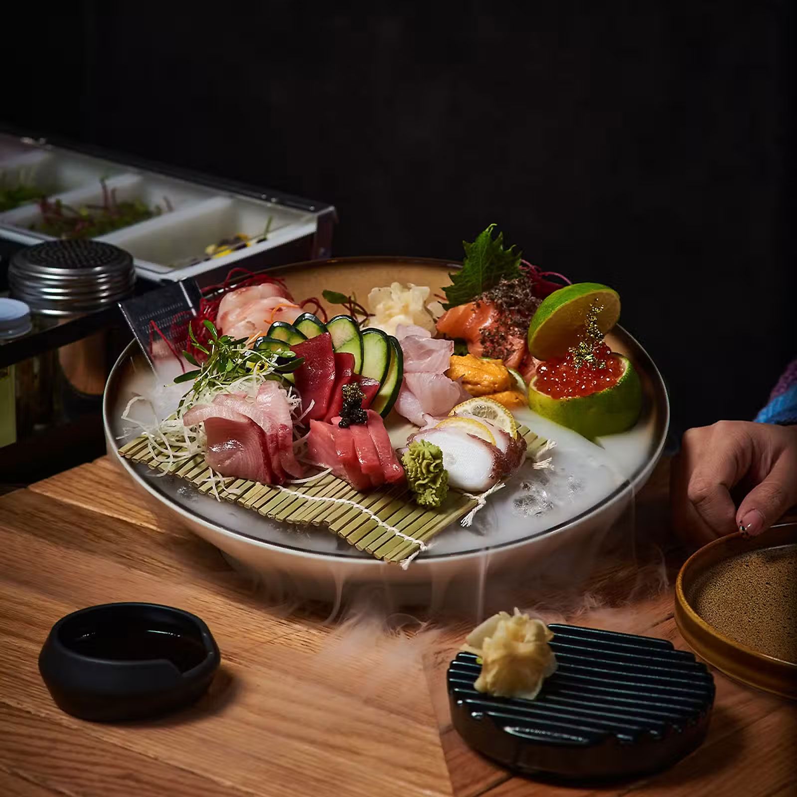 Plato de sushi con sashimi, nigiri y guarniciones sobre una mesa de madera.