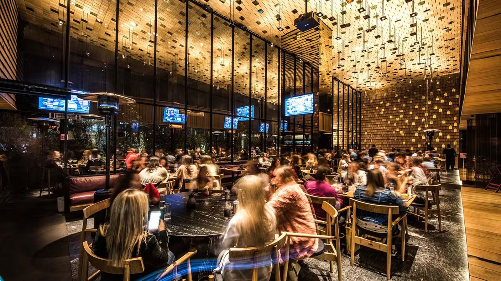 Interior de restaurante abarrotado con iluminación cálida, decoración colgante y comensales sentados en mesas.