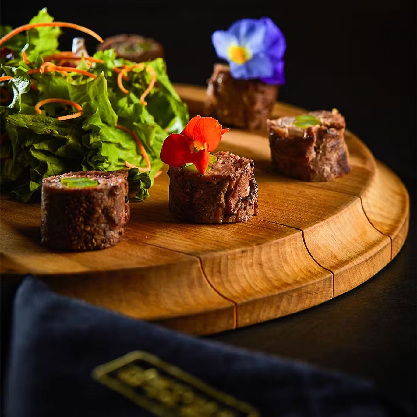 Bocaditos de postre de chocolate sobre una tabla de madera con hojas verdes y flores comestibles.