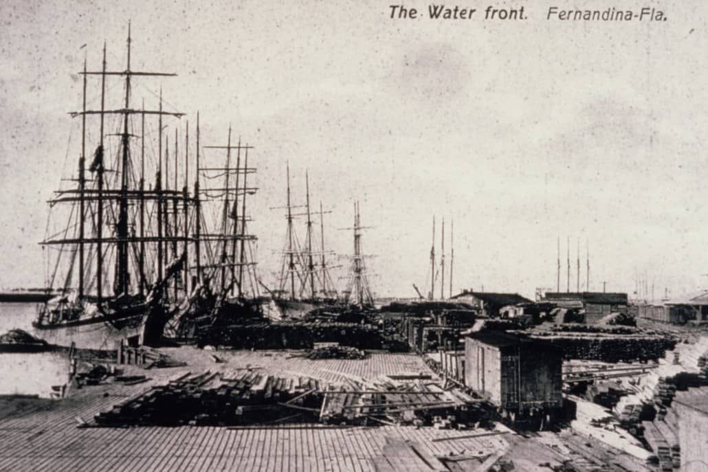 Waterfront scene with tall ships docked at a wooden pier.