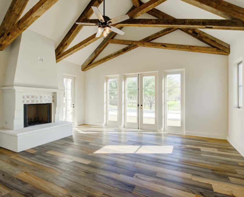 Bright living room with white walls, wood beams, fireplace, French doors, and wood flooring.